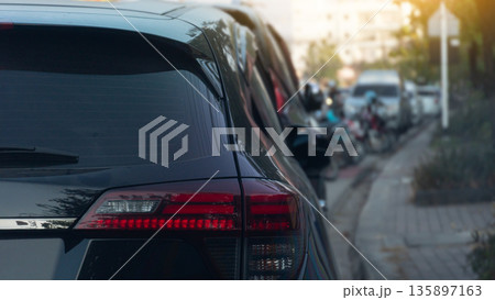 Rear side of black car parking side of road. with blurred of car and motorcycle is parked in front. sidewalks and trees in the dim light. Rear side of black car parking side of road. with blurred of car and motorcycle is parked in front. sidewalks and trees in the dim light. 135897163
