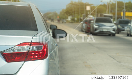 Rear side of silver car with turn on brake light on concrete road. Cars are parked waiting at the traffic light on the opposite side, despite the clear traffic conditions. Rear side of silver car with turn on brake light on concrete road. Cars are parked waiting at the traffic light on the opposite side, despite the clear traffic conditions. 135897165