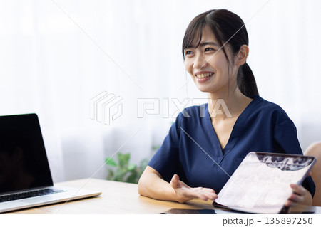 レントゲン画像が表示されたタブレットを手に患者と話す医療用スクラブを着た若い女性 135897250