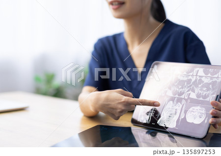 医療用スクラブを着た女性が指さすタブレットに表示されたレントゲン画像 135897253