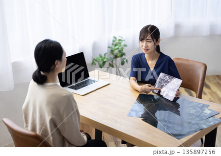 レントゲン画像が表示されたタブレットを手に患者と話す医療用スクラブを着た若い女性 135897256