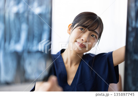 レントゲン画像を見る紺色の医療用スクラブを着た若い日本人女性 レントゲン画像を見る紺色の医療用スクラブを着た若い日本人女性 135897745