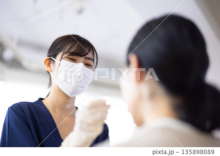 歯科用の器具を持って患者の歯をチェックする若い歯科医師の女性 歯科用の器具を持って患者の歯をチェックする若い歯科医師の女性 135898089