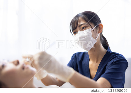 歯科用の器具を持って患者の歯をチェックする若い歯科医師の女性 歯科用の器具を持って患者の歯をチェックする若い歯科医師の女性 135898093