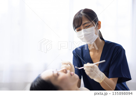 歯科用の器具を持って患者の歯をチェックする若い歯科医師の女性 135898094