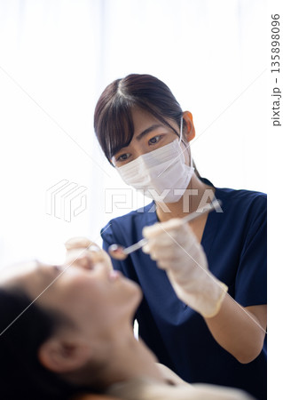 歯科用の器具を持って患者の歯をチェックする若い歯科医師の女性 歯科用の器具を持って患者の歯をチェックする若い歯科医師の女性 135898096