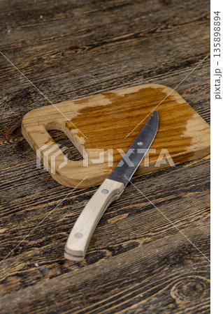 An empty cutting board is wet after food and a sharp knife, a sharp steel knife is lying on a wooden cutting board wet from water 135898894