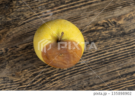 a whole yellow apple with a orange spot during rotting, one rotting apple on a black wooden table made of pine wood a whole yellow apple with a orange spot during rotting, one rotting apple on a black wooden table made of pine wood 135898902