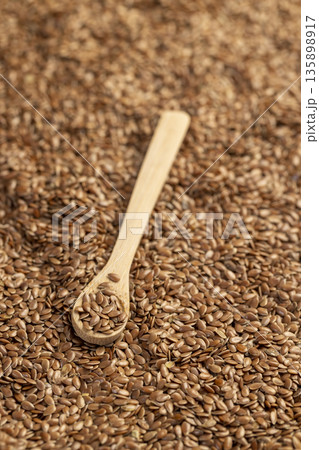 flax seeds for sowing in a wooden spoon, a large number of light brown flax seeds and a spoon with seeds 135898917