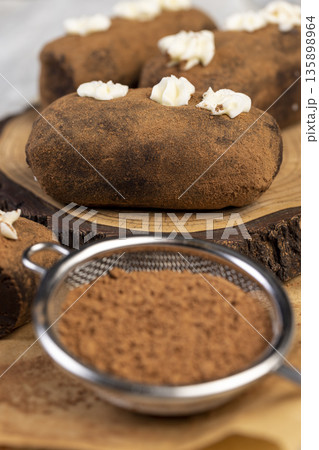 sweet brown pastry potatoes are lying on a serving board and paper, sweet classic cake from butter and a large amount of cocoa mixed with sponge cake and cognac, cocoa powder nearby sweet brown pastry potatoes are lying on a serving board and paper, sweet classic cake from butter and a large amount of cocoa mixed with sponge cake and cognac, cocoa powder nearby 135898964