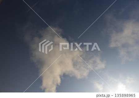 white smoke coming from a wide pipe against a blue sky background, white steam from a pipe during heating of a large industrial premises in cold weather white smoke coming from a wide pipe against a blue sky background, white steam from a pipe during heating of a large industrial premises in cold weather 135898965