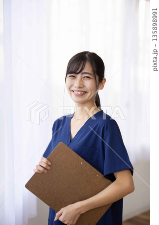 バインダーを持って微笑む紺色のスクラブを着た若い女性 135898991