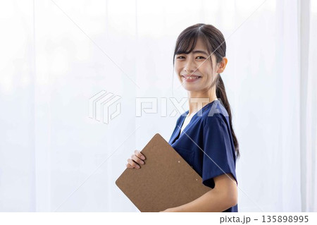 バインダーを持って微笑む紺色のスクラブを着た若い女性 バインダーを持って微笑む紺色のスクラブを着た若い女性 135898995