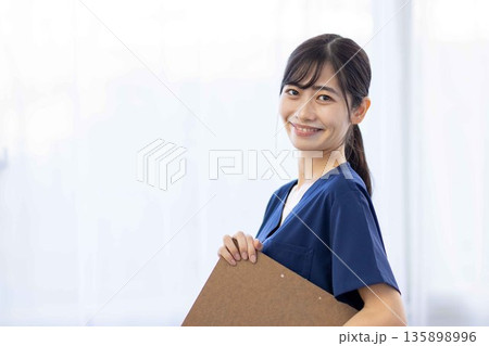 バインダーを持って微笑む紺色のスクラブを着た若い女性 135898996