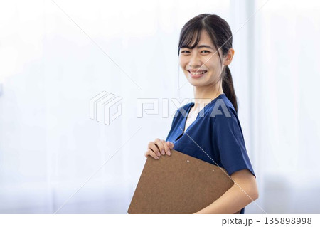 バインダーを持って微笑む紺色のスクラブを着た若い女性 バインダーを持って微笑む紺色のスクラブを着た若い女性 135898998