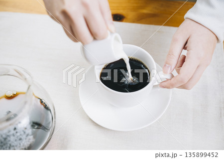コーヒーにミルクを注ぐ女性の手 135899452