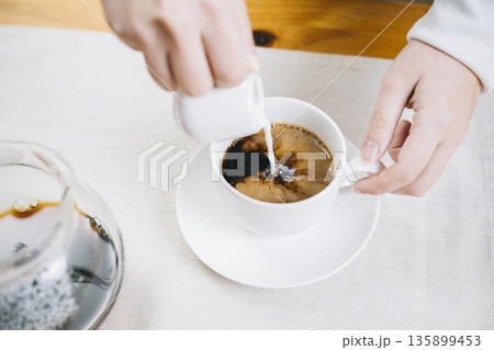 コーヒーにミルクを注ぐ女性の手 135899453