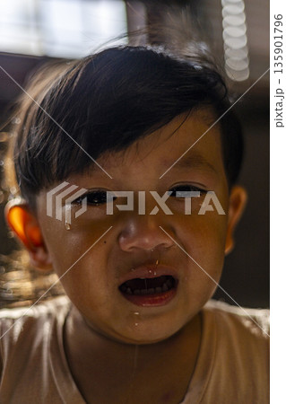 Crying Toddler With Runny Nose, A tender photo of crying toddler with runny nose, tears on flushed cheeks and small hands wiping face in light, for child health or emotional care documentary. Crying Toddler With Runny Nose, A tender photo of crying toddler with runny nose, tears on flushed cheeks and small hands wiping face in light, for child health or emotional care documentary. 135901796