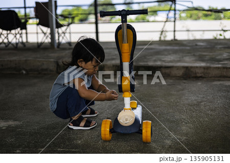 Focused Toddler Fixing Scooter, A sharp ad photo of toddler fixing scooter, tiny hands on tools in bright light, perfect for child growth campaign or curious mechanic documentary. 135905131