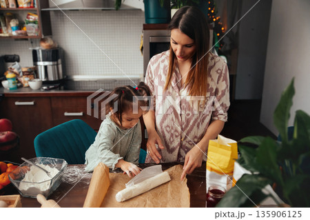 Mother and daughter prepare dough together in a kitchen, enjoying baking fun and learning new skills during the afternoon Mother and daughter prepare dough together in a kitchen, enjoying baking fun and learning new skills during the afternoon 135906125