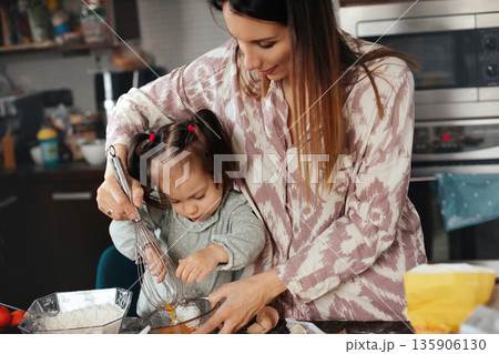 Mother and child prepare a dessert together in the kitchen during a sunny afternoon, enjoying a fun and educational moment while mixing ingredients Mother and child prepare a dessert together in the kitchen during a sunny afternoon, enjoying a fun and educational moment while mixing ingredients 135906130