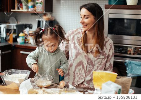 Mother and daughter make cookies together in kitchen while enjoying time spent with each other during the afternoon Mother and daughter make cookies together in kitchen while enjoying time spent with each other during the afternoon 135906133