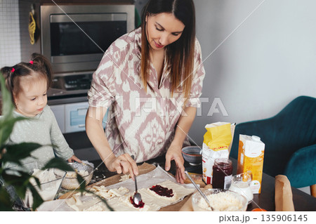 Woman prepares dough with her child by her side in a kitchen during the afternoon, enjoying a baking activity together with various ingredients around 135906145