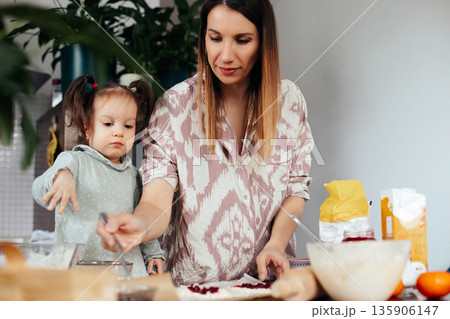 Mother and daughter prepare food together in a kitchen as they make pastries with various ingredients on the table 135906147