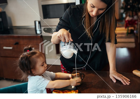Mother pours milk into childs cup during morning routine in cozy kitchen Mother pours milk into childs cup during morning routine in cozy kitchen 135906166