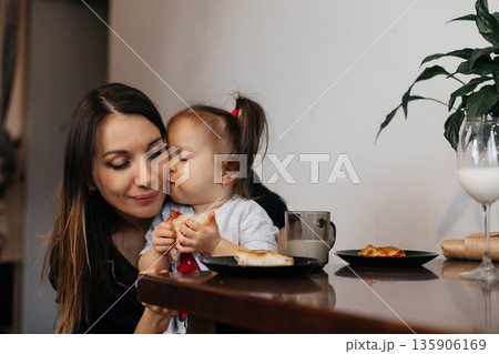 Mother and daughter share a snack in their cozy kitchen during the morning Mother and daughter share a snack in their cozy kitchen during the morning 135906169