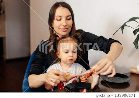 Mom and child share snack time together in a cozy indoor space while enjoying tasty food and bonding over a fun activity during the afternoon hours 135906171