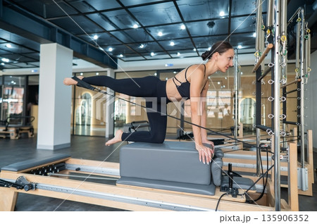 Caucasian woman doing leg exercise on reformer machine. Caucasian woman doing leg exercise on reformer machine. 135906352