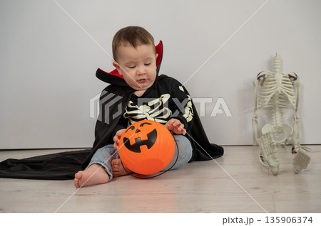 Cute caucasian boy in dracula halloween costume holding candy basket on white background. Cute caucasian boy in dracula halloween costume holding candy basket on white background. 135906374