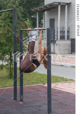 A young woman exercises on horizontal bars outdoors. A young woman exercises on horizontal bars outdoors. 135906432