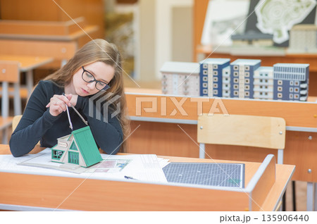 Caucasian young woman making a model of a building. Student of the construction university. Caucasian young woman making a model of a building. Student of the construction university. 135906440