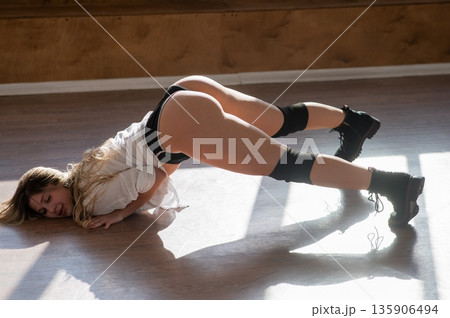 A young woman dances twerk in short shorts on the floor. A young woman dances twerk in short shorts on the floor. 135906494