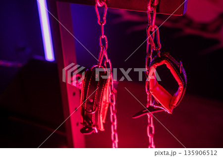 A close-up of BDSM equipment. Leather handcuffs on chains. 135906512