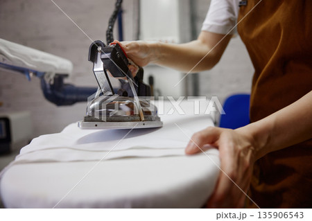 A woman is ironing a freshly laundered white shirt on a board A woman is ironing a freshly laundered white shirt on a board 135906543