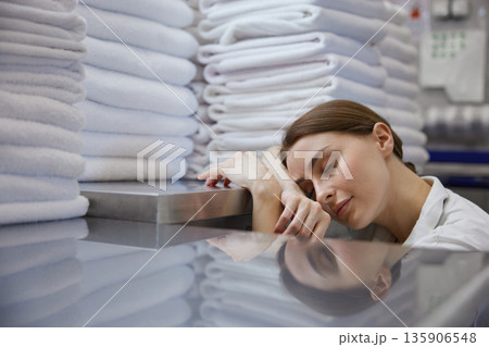 A woman is peacefully sleeping in front of a large stack of towels 135906548