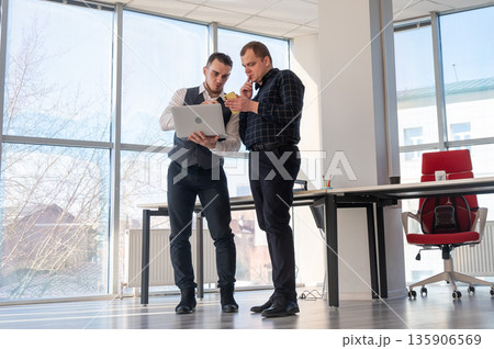 Two Caucasian men looking at a laptop and discussing work.  135906569