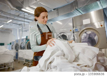Female worker is carefully folding clean towels in a bustling laundromat 135906636