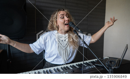Caucasian woman singing into microphone and playing synthesizer and recording herself on laptop.  135906849