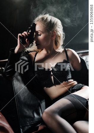 A Caucasian woman poses with a gun on a leather sofa.  135906868