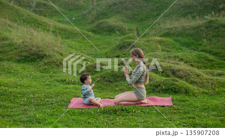 Caucasian woman doing yoga with her little son outdoors.  135907208