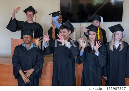 Young multinational people in graduation gowns stand at the lectern.  135907227