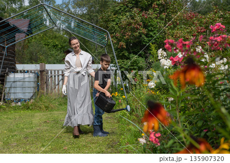 Caucasian woman and her son watering flowers in the garden.  135907320