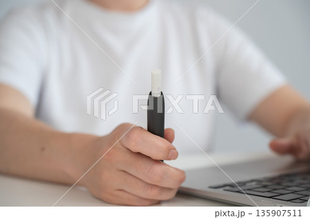 A woman smokes an electronic cigarette while working on a laptop. Tobacco heating system. 135907511