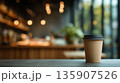Coffee cup sits on a table as cafe lights shine softly in the background during daytime hours 135907526
