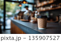 Warm coffee sits on a table in a busy cafe with blurred people and shelves in the background 135907527