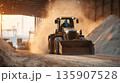 Construction equipment moves sand and gravel inside large warehouse at sunset in an industrial area 135907528